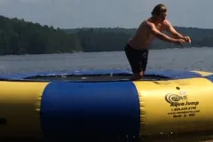 Someone bouncing on the blue and yellow Rave water trampoline on the lake