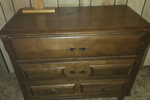 A wooden three-drawer dresser against a pine-panelled wall