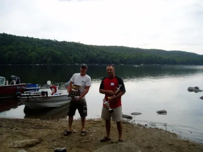 One man handing a trophy to the another man on a beach at the annual corn roast