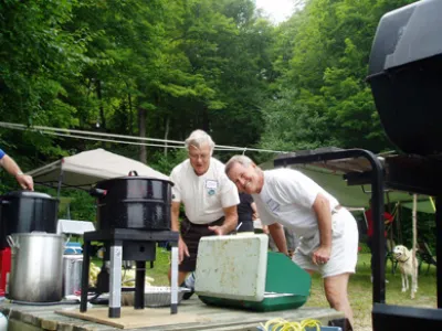 Two men standing over a BBQ at the annual corn roast