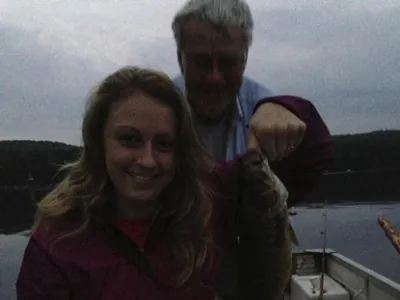 Jordan sitting in a boat and holding a fish at dusk