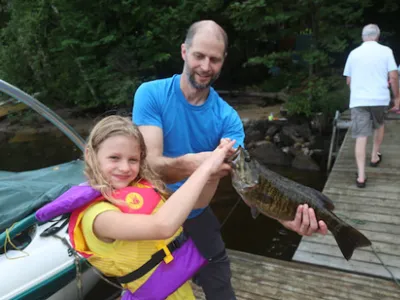 Sophia Edey wearing a lifejacket and holding up a bass while standing on a dock