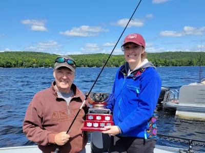 Chloe and Mark ristow in a boat on Percy Lake holding the Bass Tournament fishing trophy.