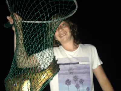 Julian Tilman holds a net up with a bass fish in it.