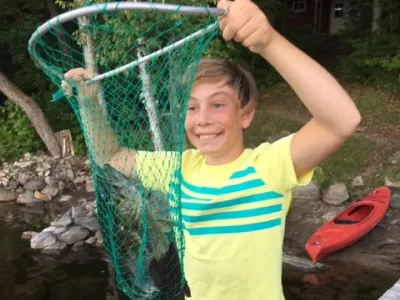 Young man holding up a fishing net with a bass inside