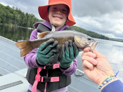 A young Odin wearing gloves holds up a bass while standing in a boat.