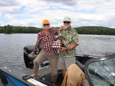 Two men in a boat, holding a fishing trophy.