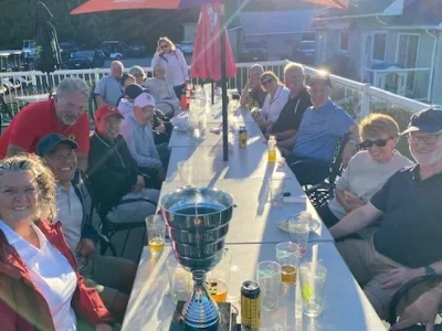 Golfers at dinner around a long table on the clubhouse patio, with the trophy