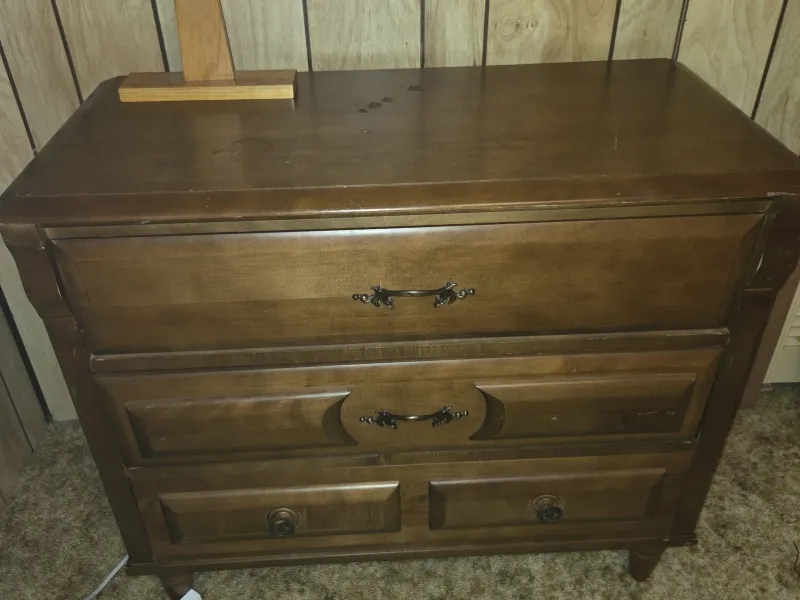 A wooden three-drawer dresser against a pine-panelled wall