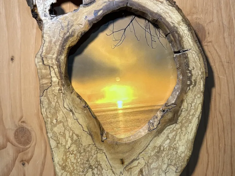 A photo of the sun rising over Percy Lake, set in a hollowed-out, polished tree-trunk frame