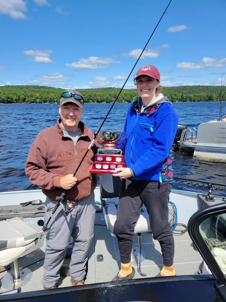Chloe and Mark ristow in a boat on Percy Lake holding the Bass Tournament fishing trophy.