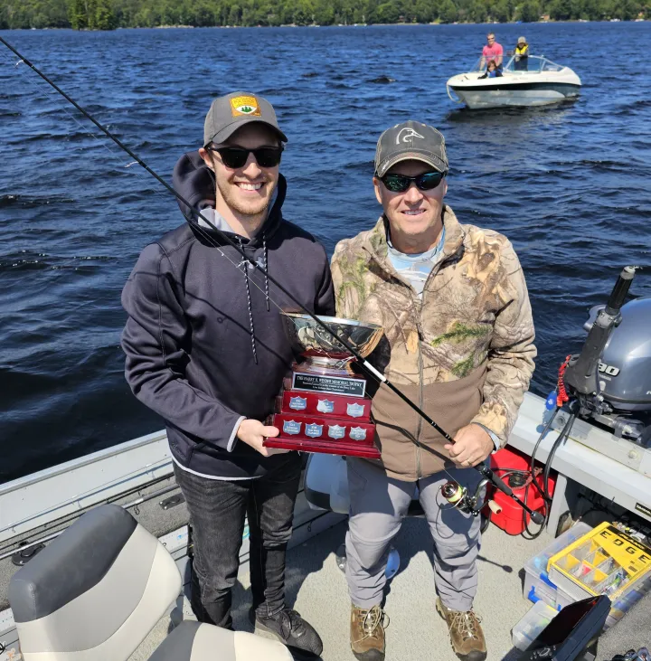 Mark and Connor Ristow stand in their boat holding up a fishing trophy.